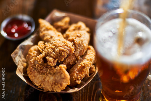 focus on fried chicken tenders in basket with beer being poured in foreground