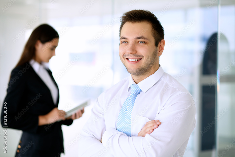 Smiling businessman in office with colleagues in the background Smiling businessman in office with colleagues in the background