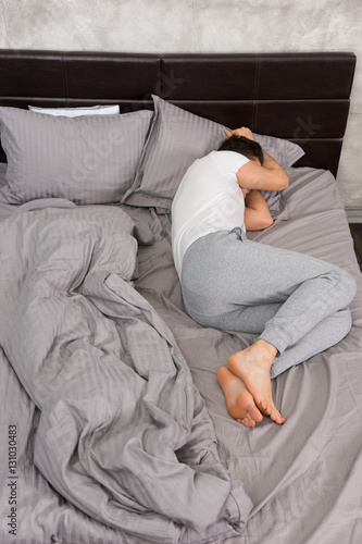 Young tired man sleeping without blanket in stylish bed in grey