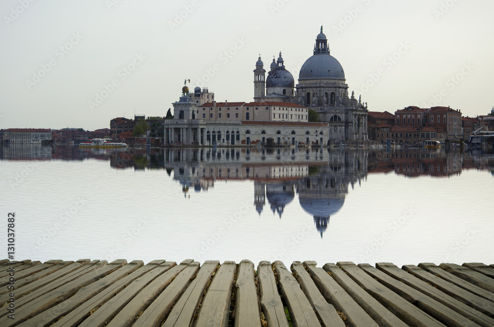 Fototapeta premium Fine art image with Grand Canal and Basilica Santa Maria della Salute, reflected on the water surface, with wood planks floor for foreground, Venice, Italy.