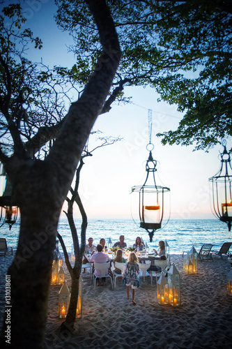 A group of friends and family eat dinner at a private table on a beach, surrounded by candle lanterns. Mexico.