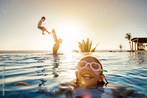 Father throws son in the pool with daughter in forground wearing goggles and laughing