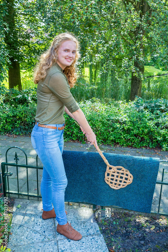 Young dutch woman beating door mat with carpet beater photo