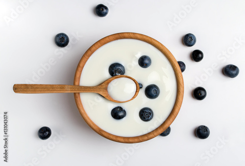 White yogurt in natural wooden bowl with blueberries. Top view on white background.