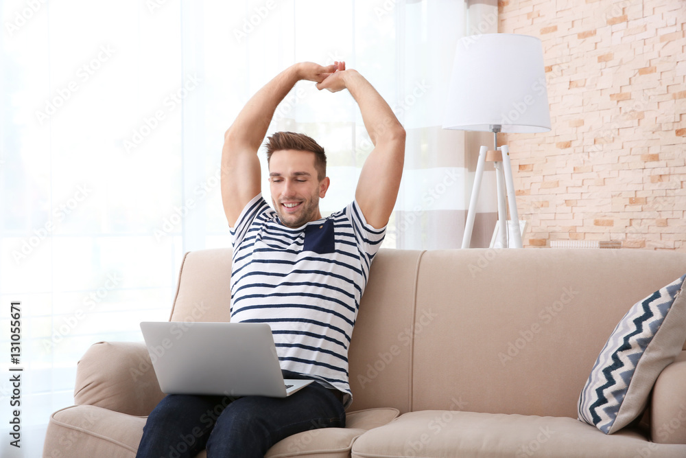 Young man with laptop on sofa in the room Young man with laptop on sofa in the room