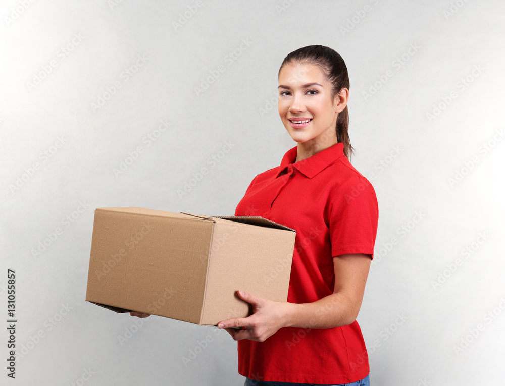 Pretty warehouse worker with cardboard box on light background Pretty warehouse worker with cardboard box on light background