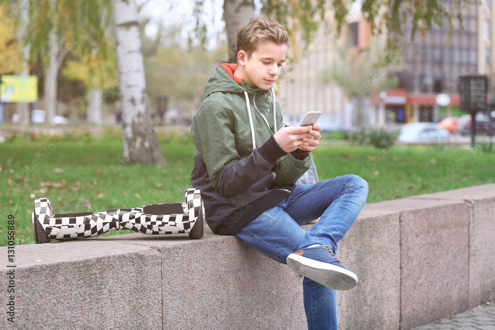 Obraz premium Teenager sitting on parapet with mobile phone and gyroscooter in autumn day