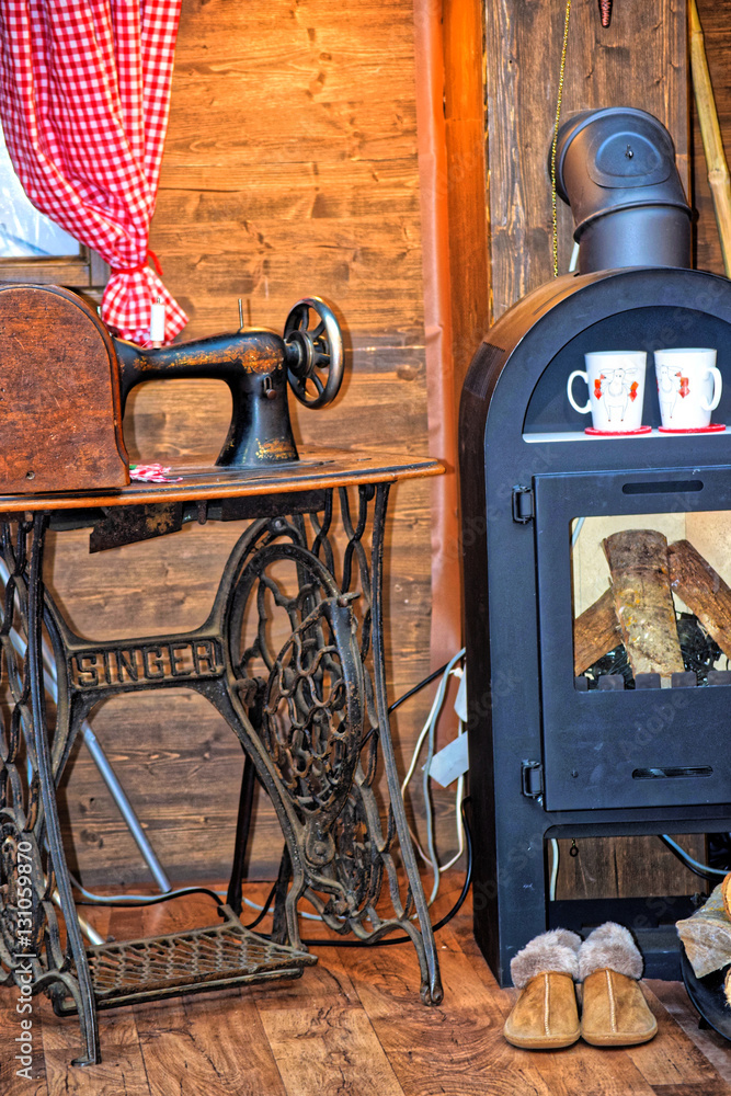 Fototapeta premium Old sewing machine, and a fireplace, lay next to the firewood. In the fireplace warm
