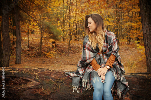 Fototapeta Naklejka Na Ścianę i Meble -  Beautiful young woman sitting on wood log in autumn park