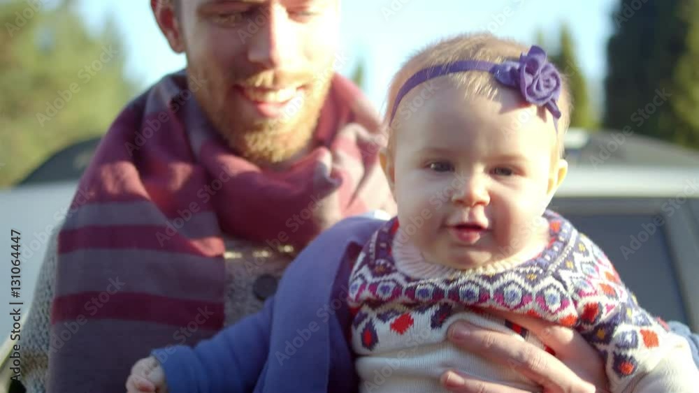 A baby smiles while her dad holds her and her mom puts her jacket on A baby smiles while her dad holds her and her mom puts her jacket on