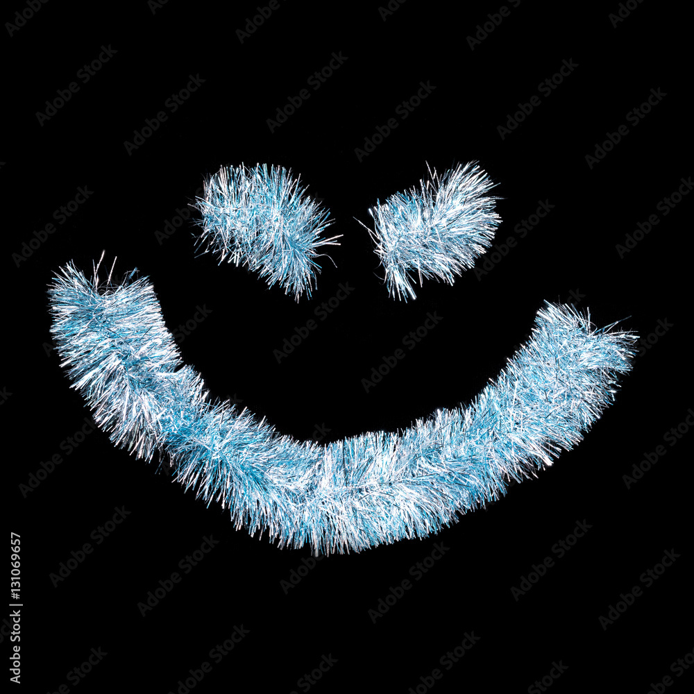 Fototapeta premium Smiling face made of blue tinsel on a black background. Isolated