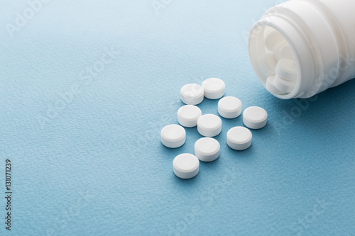 Pills spilling out of pill bottle on blue background. with copy
