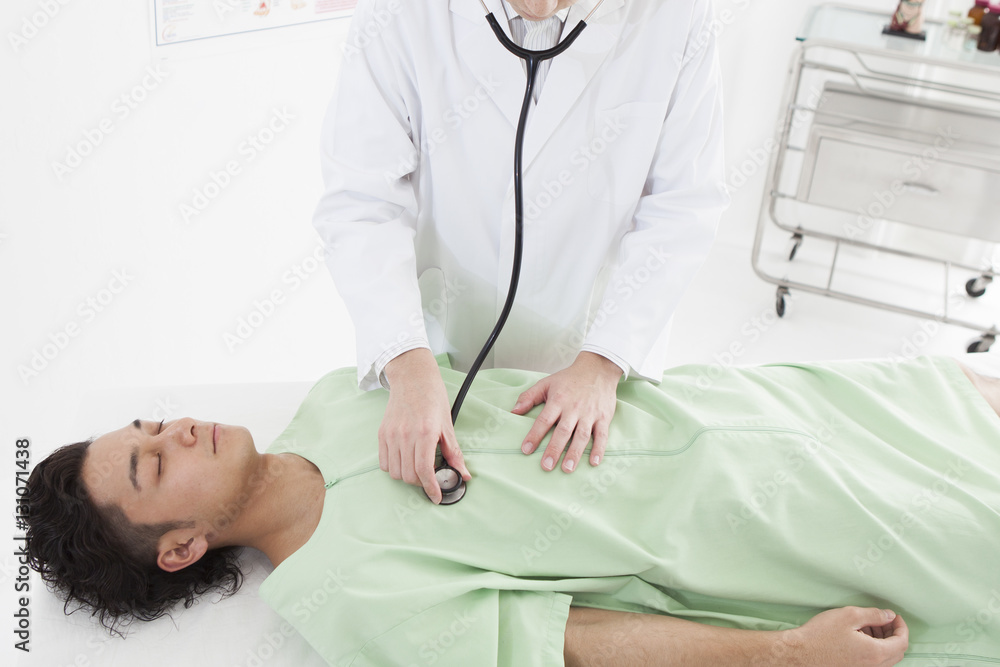 The doctor is applying a stethoscope to the stomach of a man The doctor is applying a stethoscope to the stomach of a man