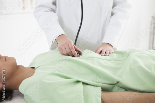 The doctor is applying a stethoscope to the stomach of a man