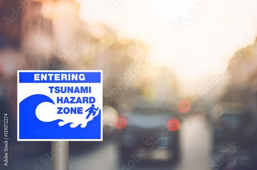 Tsunami hazard zone warning sign on blur traffic road with colorful bokeh light abstract background.