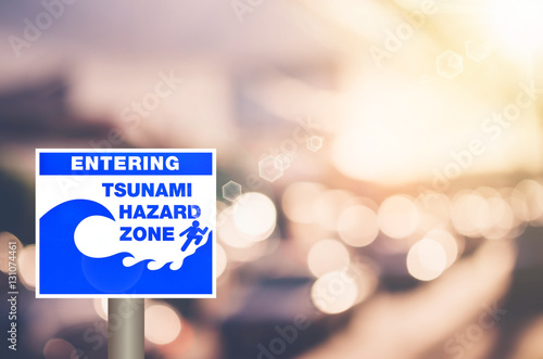 Tsunami hazard zone warning sign on blur traffic road with colorful bokeh light abstract background.