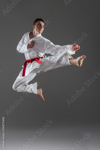 Attractive young sportsman practice in karate isolated over grey background