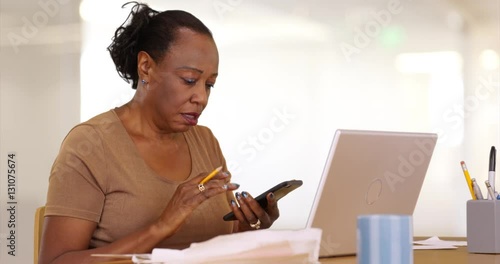 An older black woman works on her laptop with her paperwork. An elderly African American woman does her taxes on her computer