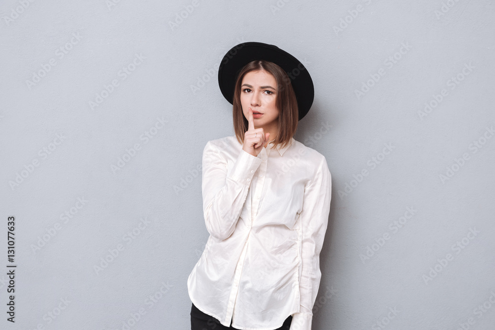 Portrait of a young woman in hat showing silence gesture Portrait of a young woman in hat showing silence gesture