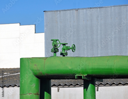 Green painted metal pipe with two valves on the background of the industrial enterprise.