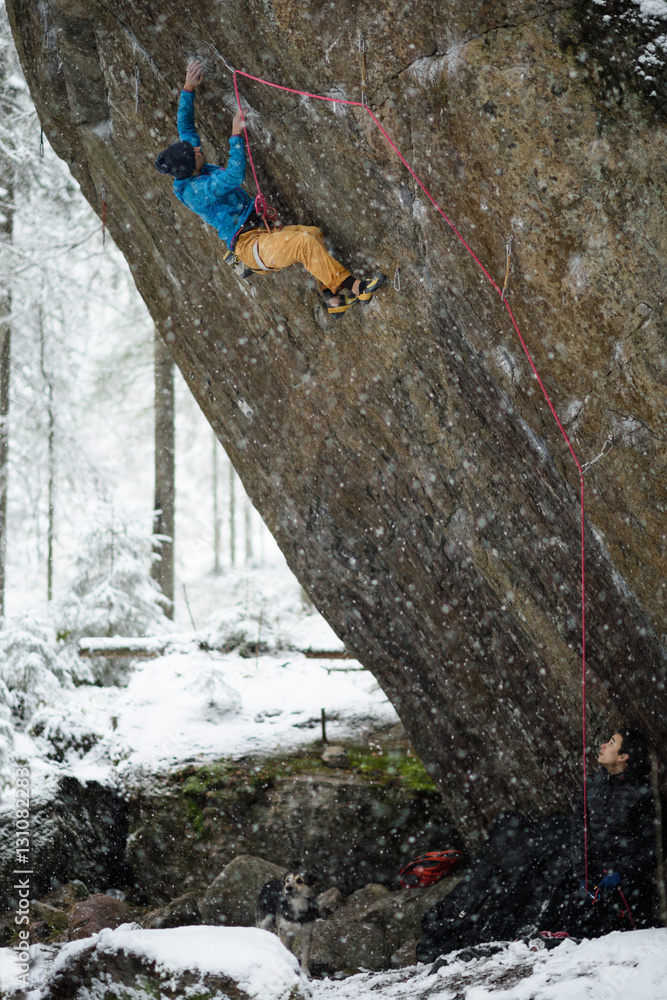 Obraz premium Extreme winter sport climbing. Young male rock climber on a rock wall. Snowy forest on the background.