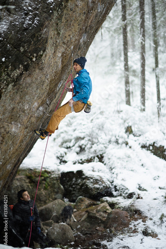 Outdoor winter sport. Rock climber struggles to climb a challenging cliff. 