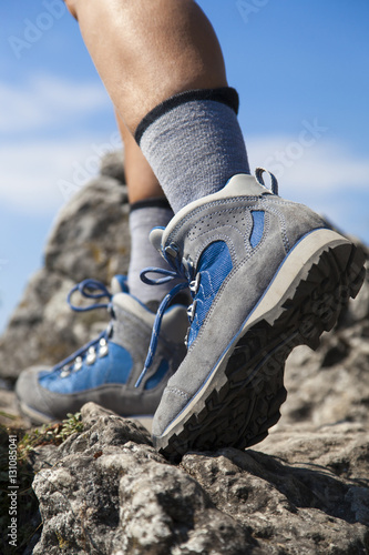 Close up of hiking boots and legs climbing up rocky trail and reaching the top of a mountain