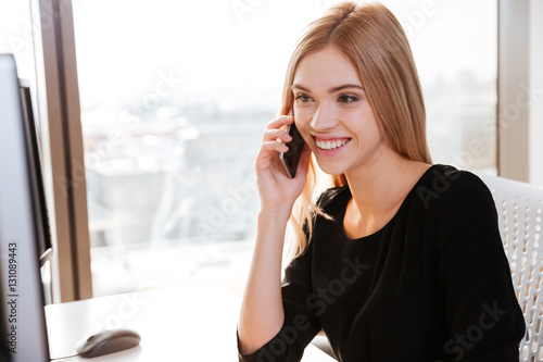 Smiling lady worker sitting in office while talking by phone