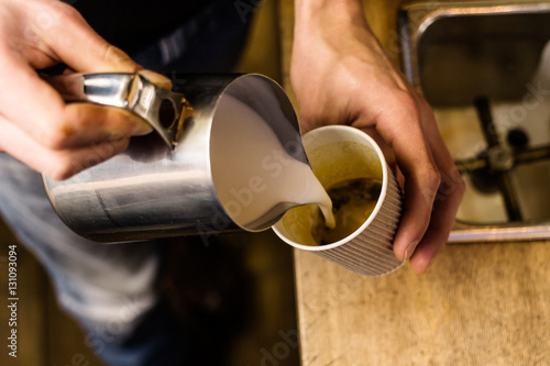 Barista pouring milk to takeaway coffee