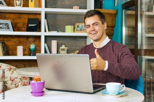 Canvas Print A young man in a cafe with laptop smiling and showing thumb up