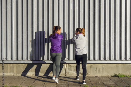 Two sporty women stretching calf for warming up before urban fitness workout or running. Female athletes exercising outside.