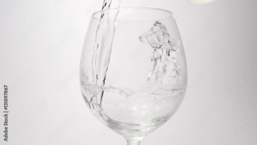 SLOW MOTION: Water pour into a wine glass on a white background SLOW MOTION: Water pour into a wine glass on a white background
