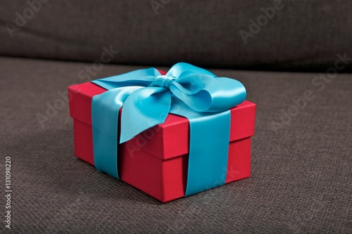 gift present red box with blue ribbon on brown sofa seat    © Q