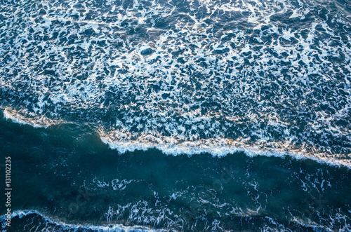 Aerial view of the tidal waves reaching the empty sandy beach in winter