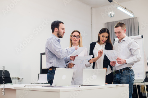 Group of four diverse men and women in casual clothing talking in office