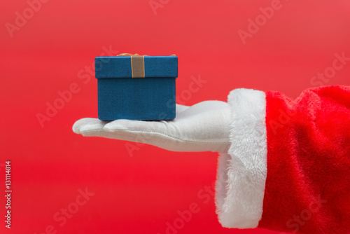 Santa Claus hand holding Christmas Gift box over red background
