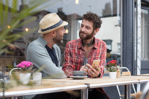 Gay couple sat sharing content on phone outside a cafe © Fergus Coyle