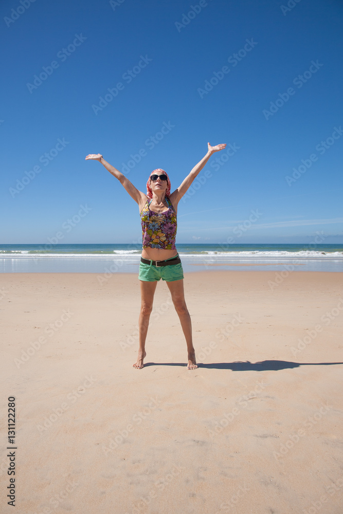 woman with headscarf green shorts opening arms at a beach
woman with headscarf green shorts opening arms at a beach