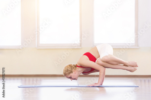 Young woman in white doing yoga pose arm balance