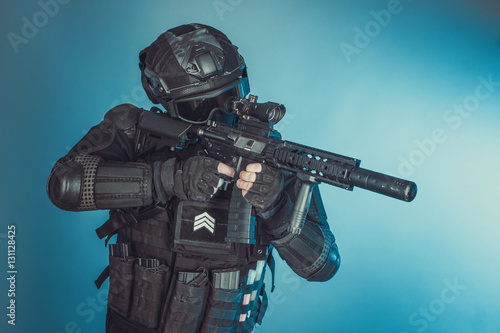 Member of the SWAT squad with an assault rifle in a black uniform on blue background. Special weapons and tactics. Special Forces.