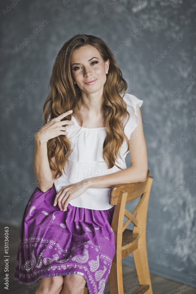 Fototapeta premium A slender girl in a purple skirt sitting on a chair 6909.