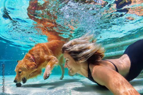 Underwater action. Smiley woman play with fun, training golden retriever puppy in swimming pool - jump and dive. Active water games with family pet, popular dog breed like companion on summer vacation