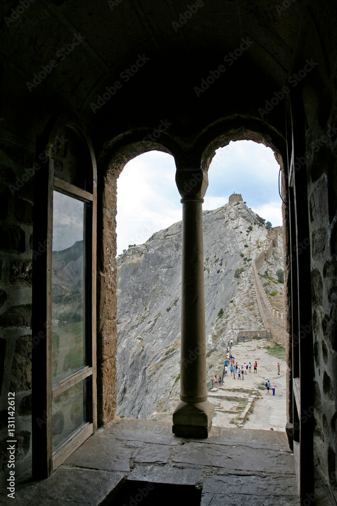 The view from the opened arch window to the medieval tower and the stony wall on the top of the limestone cliff. This photo was taken in fortress Soldaia near town Sudak, Crimea.