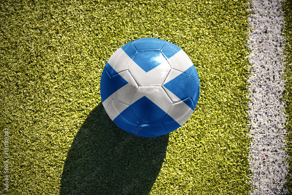 Naklejka premium football ball with the national flag of scotland lies on the field