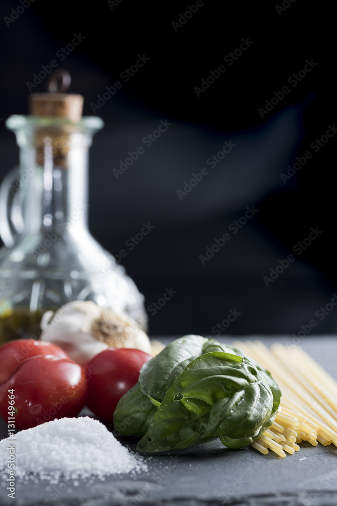 ingredients for a pasta with spaghetti, tomato, basil and extra virgin olive oil on black plate ingredients for a pasta with spaghetti, tomato, basil and extra virgin olive oil on black plate