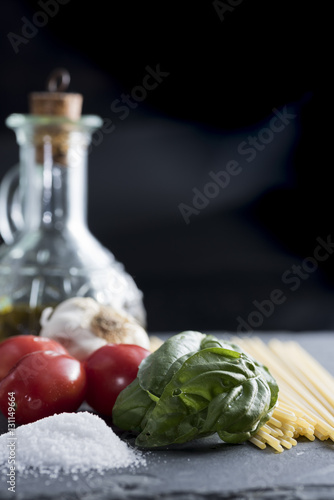 ingredients for a pasta with spaghetti, tomato, basil and extra virgin olive oil on black plate