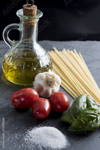ingredients for a pasta with spaghetti, tomato, basil and extra virgin olive oil on black plate
