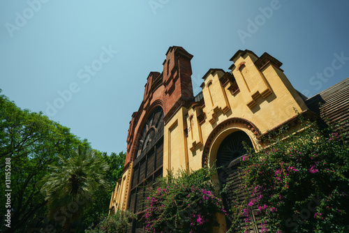 Wide angle view of brick and grid facade of old building with clean blue sky behind and purple flowers of bindweed on it, park area, sunny summer day, Barcelona, Spain photo