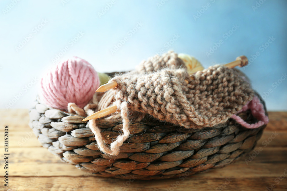 Knitting yarn and needles in wicker basket on wooden table