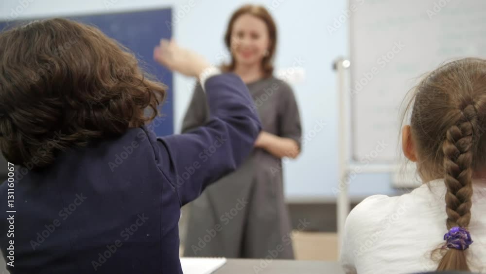 Classmates on school - children girls sits on table and holding pens during the teacher explains the lesson Classmates on school - children girls sits on table and holding pens during the teacher explains the lesson